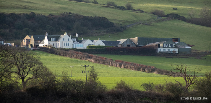 Rural Scottish hillside with traditional white stone houses and farm buildings nestled in rolling green fields.