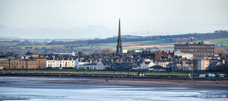 Scottish riverside town skyline with church spire and historic stone buildings reflected in tidal waters.