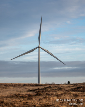 Wind turbine standing alone in an arid landscape beneath a partly cloudy sky.