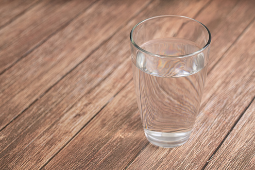 A glass of water positioned on a wooden surface with visible wood grain texture.