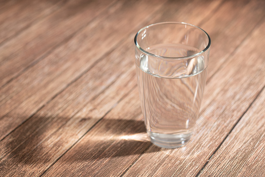 Clear glass filled with water on wooden surface with dramatic shadow.