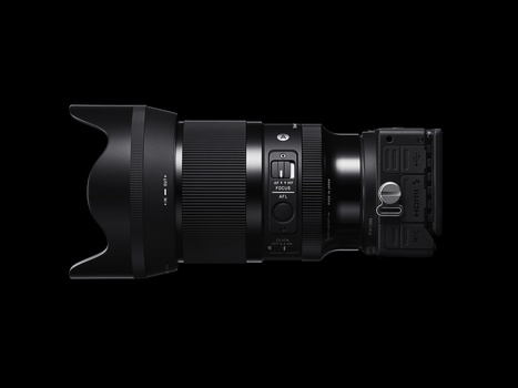 Side profile of a telephoto lens with hood, controls, and rear mount visible against black background.