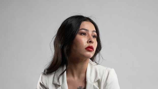 Woman in cream blazer gazing upward against neutral background.