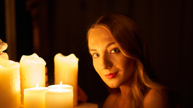 Woman's face illuminated by warm candlelight against a dark background.