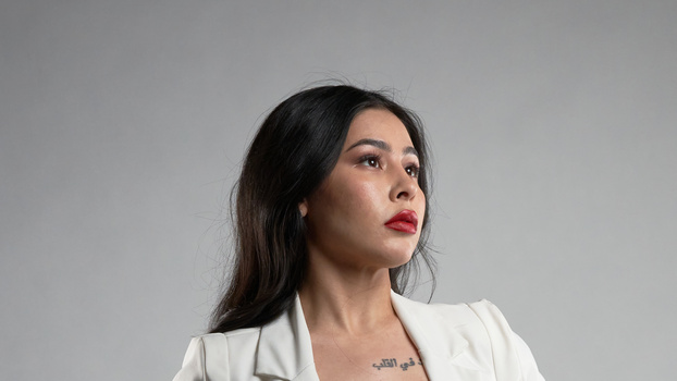 Woman with long dark hair and red lipstick gazing upward against neutral gray background.