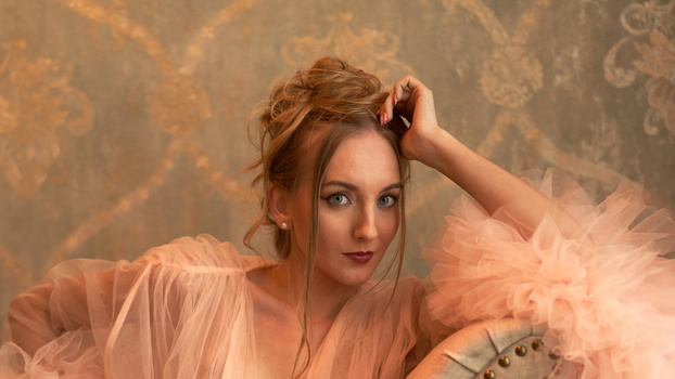 Woman in flowing peachy tulle fabric against ornate damask wallpaper backdrop.