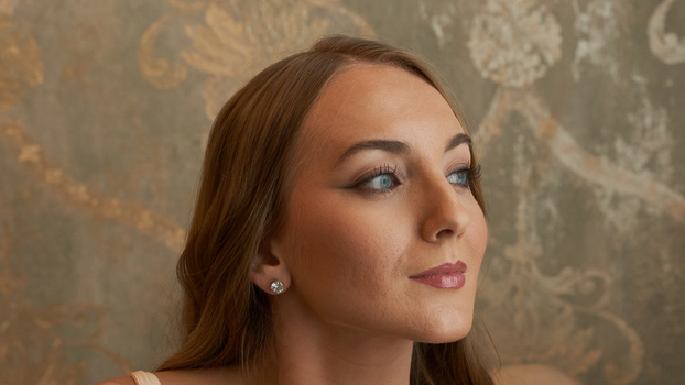 Woman with long brown hair in profile against patterned wallpaper, soft directional lighting from the left side.