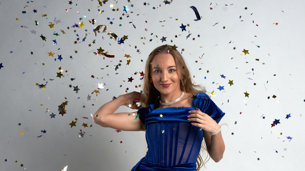Woman in blue dress tossing colorful star confetti against white background.