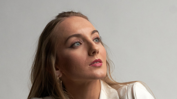 Woman with long brown hair looking upward against neutral gray background.