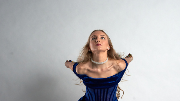 Woman in blue off-shoulder dress looking upward against white background.