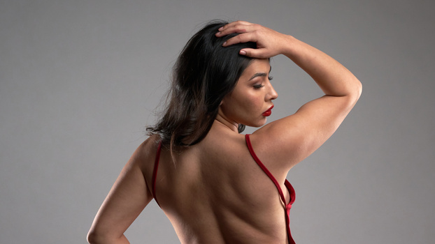 Woman in burgundy halter top photographed from behind against neutral gray background.