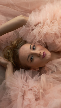 Young person lying on layered pink tulle fabric, looking directly at camera with natural expression.