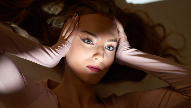 Woman with hands framing face, warm studio lighting with soft shadows and brown tones.