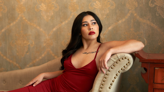 Woman in red dress reclining on upholstered chair against damask wallpaper.