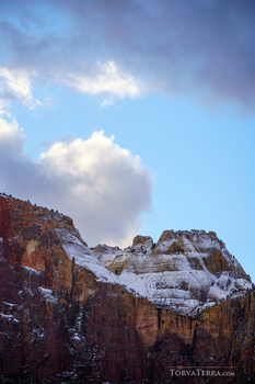 Layered desert mountains with snow patches beneath dramatic blue sky and white clouds.