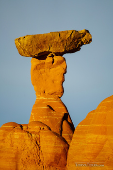 Balanced rock formation with golden-orange hue against clear blue sky.