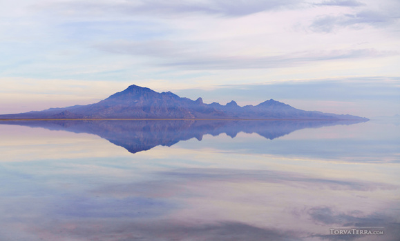 Mountain range with jagged peaks reflected in still water at sunrise or sunset.