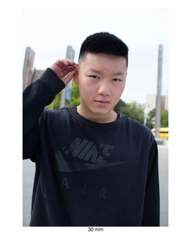 Young man in black Nike sweatshirt posing outdoors with hand near head.