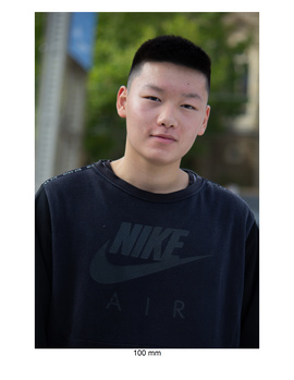 Young man wearing black Nike t-shirt against blurred green outdoor background.