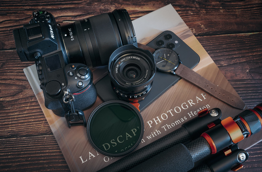 Camera gear arranged on wooden surface with photography book and accessories.