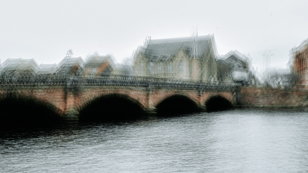 Historic stone bridge with multiple arches spanning a river, lined with period buildings in misty conditions.
