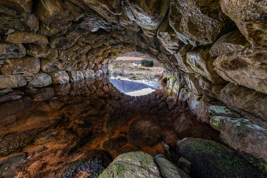 View through a cave opening toward a coastal landscape with water and distant structures.