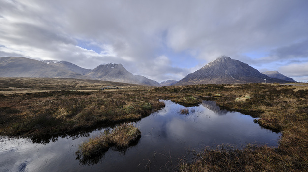 Mountain landscape with volcanic peaks reflected in still water surrounded by moorland.