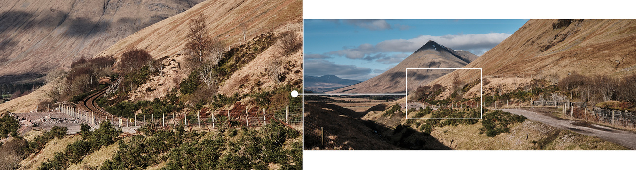 Mountain landscape with fenced hillside vegetation and distant peaked volcano under partly cloudy sky.