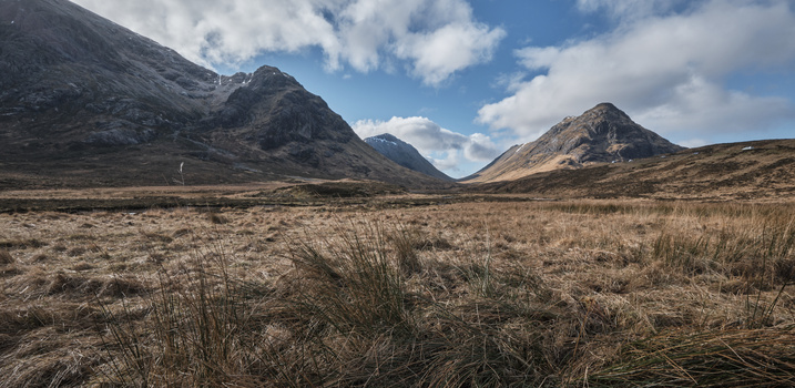Three dramatic peaks rise from a vast, barren moorland beneath a partly cloudy sky.