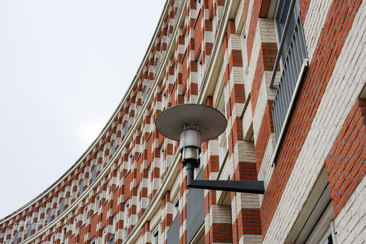 Street lamp mounted on a curved brick building facade with red and white brickwork pattern.