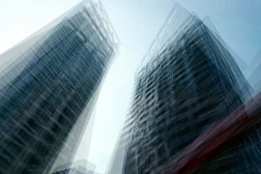 Two modern skyscrapers shot from below against a bright sky, creating a dramatic upward perspective with motion blur effect.