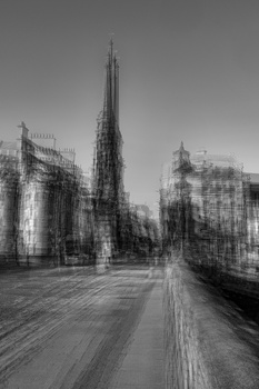 Gothic cathedral with soaring spire dominates a blurred urban street scene in monochrome.