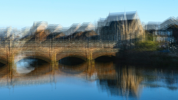 Double exposure of brick bridge with arches overlaid with residential buildings and trees reflected in still water.