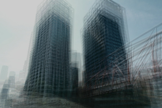 Two tall residential towers shrouded in heavy fog with blurred foreground elements and cityscape in background.
