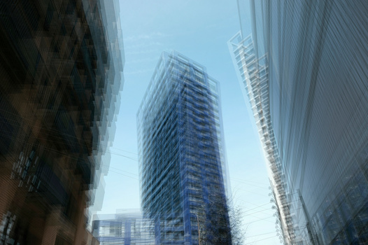 Upward view of modern high-rise buildings converging toward clear blue sky.