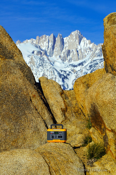 Snow-capped mountain peaks framed between golden granite boulders in sharp focus foreground.