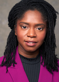 Professional headshot of a woman with long dark braids wearing a magenta blazer over a dark ribbed shirt.