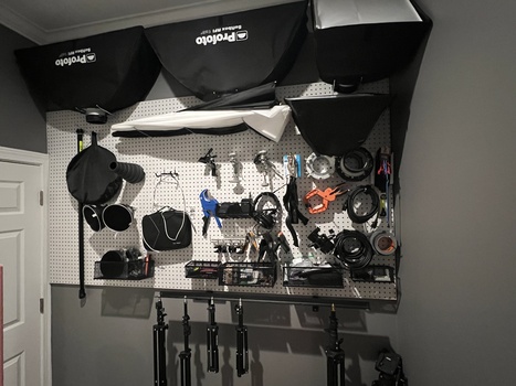 Photography studio wall-mounted pegboard organizer displaying lighting equipment, reflectors, and accessories.