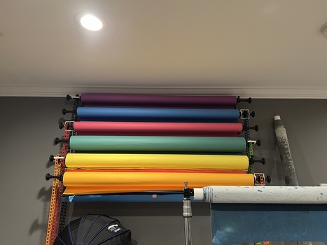 Stacked fabric backdrop rolls in various colors mounted on a horizontal rod system.