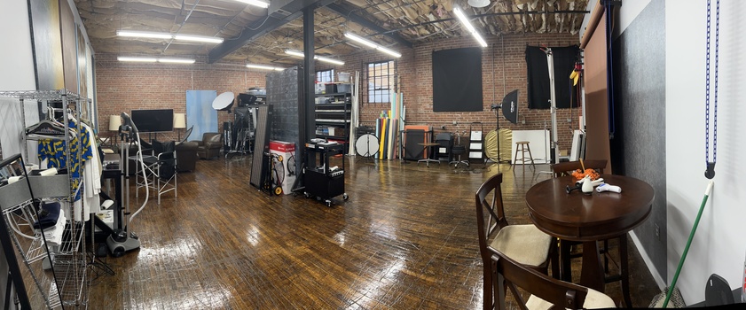 Spacious photography studio with exposed brick walls, wooden floors, and professional lighting equipment throughout the space.