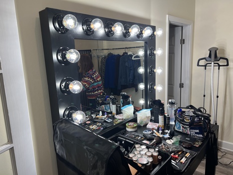 Professional vanity mirror with Hollywood-style bulbs mounted above a makeup station cluttered with cosmetics and beauty products.