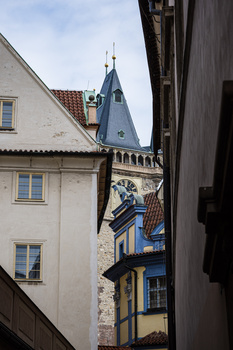 Narrow European alleyway with historic buildings, blue-roofed turret visible between white and yellow structures.