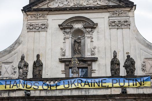 Neoclassical church facade with stone statues and blue banner reading 'HANDS OFF UKRAINE, PUTIN!'
