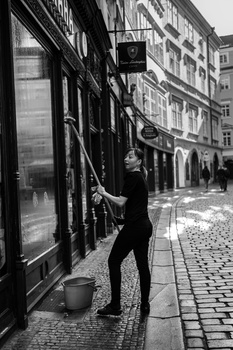 Person in dark clothing standing against storefront window on European cobblestone street.