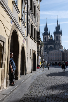 Cobblestone street lined with historic buildings frames a Gothic church with twin spires in the distance.
