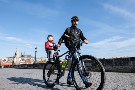 Adult cyclist with child passenger riding on urban waterfront promenade under clear sky.