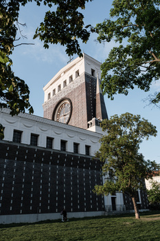 Modernist brick tower with clock face framed by tree branches and clear sky.