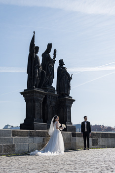 Bride and groom posing in front of a tall dark monument structure against a blue sky.