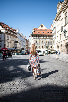 Woman walking away from camera on cobblestone plaza surrounded by historic European architecture.