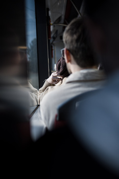 Person in white shirt viewed from behind through blurred foreground, reaching toward a dark architectural element.